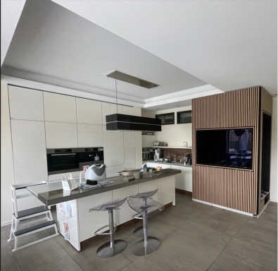Einbauküche Moderne Küche mit hellen Oberflächen, Barhockern und einem großen Fernseher.